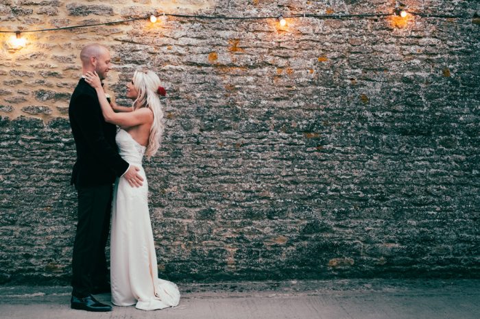 bride and groom in front of barn wall with festoon lights