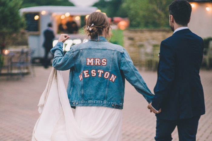 bride in denim jacket with name on the back walking towards a pizza van